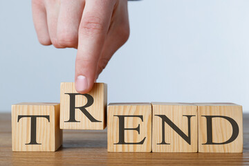 Man making word Trend with wooden cubes at table against light background, closeup
