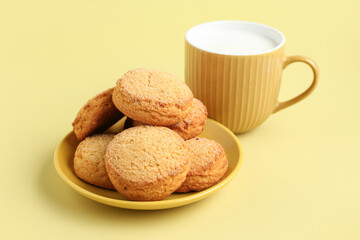 Plate with sweet cookies and cup of fresh milk on yellow background
