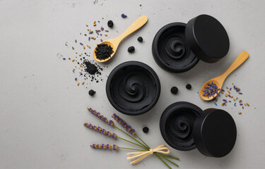 Three black containers of charcoal face mask, accompanied by wooden spoons, dried lavender, and blueberries.  A wellness and beauty concept.