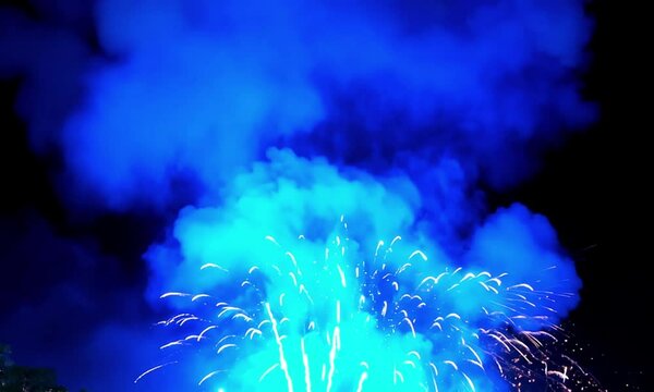 Dazzling blue fireworks exploding in the night sky with thick smoke clouds, capturing a festive celebration atmosphere, perfect for New Year, Independence Day, or joyful public events.