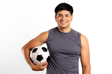 Young Latin man athlete smiling at the camera with a soccer ball under his arm, copy space