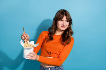 Portrait of a young woman with an expressive reaction holding noodles while wearing an orange top...