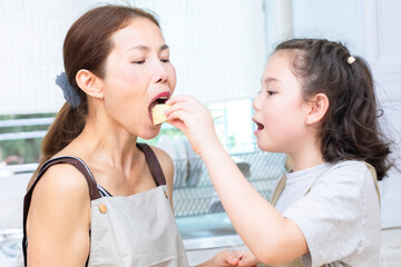 Smiling mother pouring orange juice into a glass for cheerful daughter, capturing family bonding and care, woman and child sharing a happy moment, happiness and warmth in kitchen atmosphere