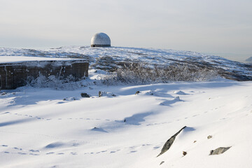 Fototapeta premium The white dome (radiotransparent shelter) of an abandoned radar station on the top of a mountain. Snowy mountain slope. Tourist attraction in the vicinity of Magadan. Magadan region, Far East Russia.