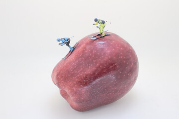 Miniature Skiers Gliding Down a Red Apple Slope Concept