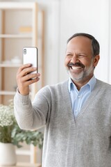 Smiling Senior Man Taking Selfie at Home: Happy Older Man with Smartphone in Modern Home Interior