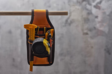 Tool belt with essential construction tools such as a measuring tape, utility cutter, pencil, and...