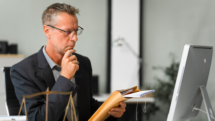 An elderly Caucasian male lawyer works at his desk in a law firm, offering legal advice and...