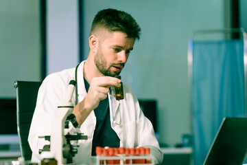 A white male scientist at a table, studying blue substances in test tubes and bottles, using a...