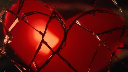A glowing red heart is seen through shattered glass, symbolizing heartbreak or emotional pain.