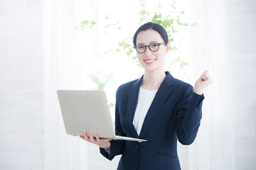 逆光の綺麗なオフィスでパソコンを持ってガッツポーズの女性