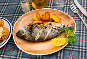 Appetizing grilled dorada fish served with baked potatoes, lemon slice and fresh parsley..