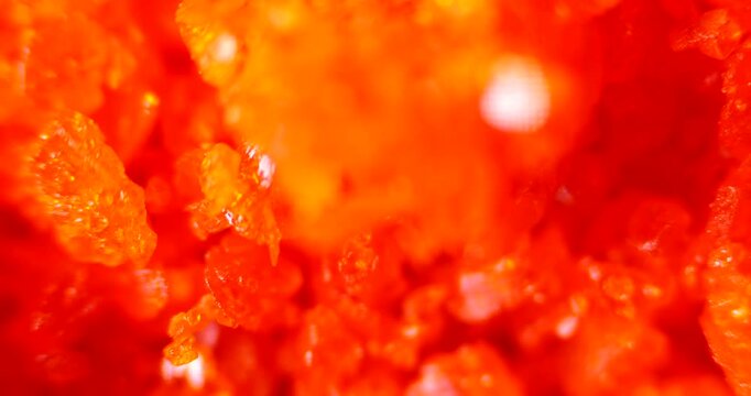 Extreme close-up of Ammonium Dichromate crystals showing intense orange geometric patterns and crystalline structures under laboratory lighting