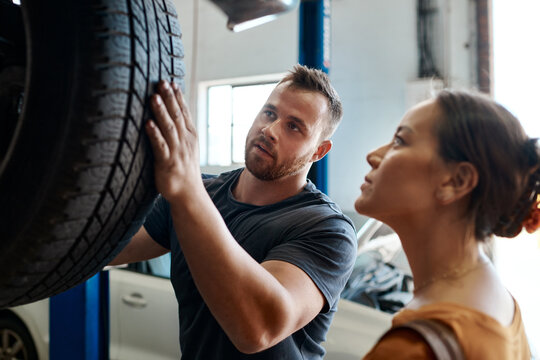 Customer, tire and mechanic in garage for maintenance, inspection and car service assessment. Woman, wheel and check in auto repair workshop for motor performance, quality assurance or vehicle safety
