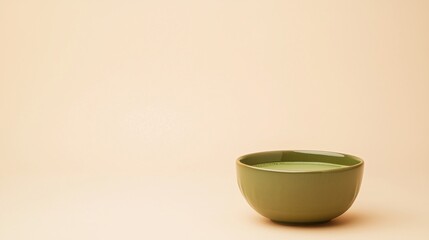 A simple green ceramic bowl filled with liquid sits on a beige background with minimalistic style.