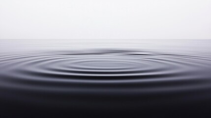 Gentle ripples expand across a calm, minimalist water surface under a pale sky.