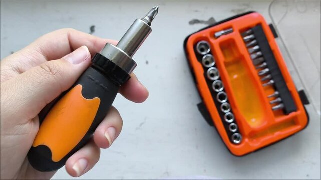 A screwdriver for screws, screws, and self-tapping screws in his hand, in the background is a container with nozzles with different threads for screwdrivers. A set of tools for screwing in screws.