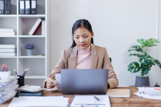 Brunette young asian businesswoman sitting at the office and using laptops for work. Confident professional female wearing business financial planning casual. - Powered by Adobe