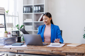 A focused asian woman accountant analyzing paperwork while calculating expenses using laptop and calculator at her office desk.
