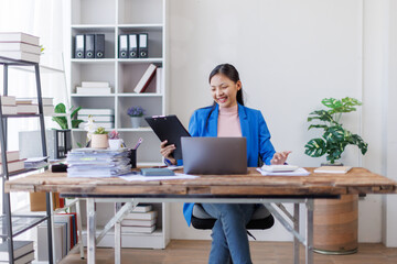 A focused asian woman accountant analyzing paperwork while calculating expenses using laptop and...