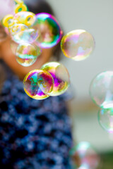 Little Asian girl playing soap bubbles outdoors in daylight