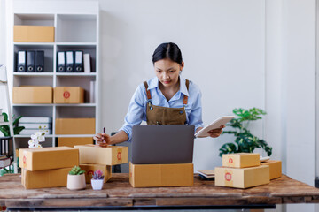 Asian woman SME business owner online shopping working on laptop computer with parcel box at home...