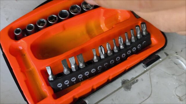 Men's hands take the screwdriver head out of the container. A screwdriver with nozzles with different threads. Screwing in the screws.