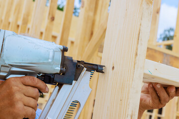 Craftsman during teamwork nail gun to fasten wooden beam at construction site
