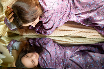 A woman in a floral robe lying on a couch while gazing at her reflection on a polished surface...