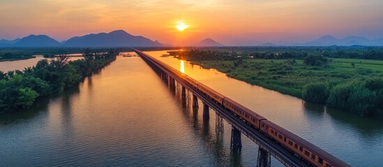 Fototapeta premium Train Crossing Bridge at Sunset Over River Landscape
