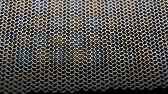 Precision laser-cut metal sheet featuring perfectly uniform microscopic oval holes rotating smoothly in extreme close-up