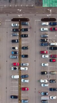 Cars lined up in Riga parking lot during sunset, vertical drone overview framing structure, sedan pulls in and people walk back to cars