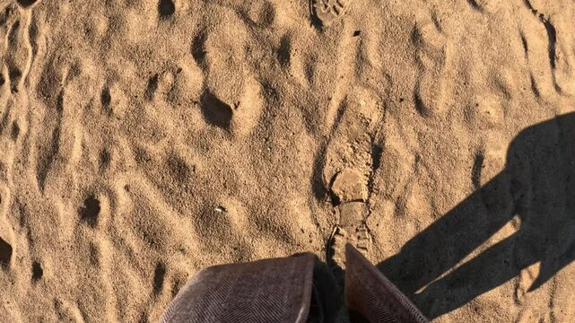 Brown leather shoe stepping on soft golden sand in sunny daylight