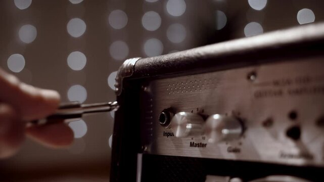 A man turns the volume knob on an electric amp to guitar