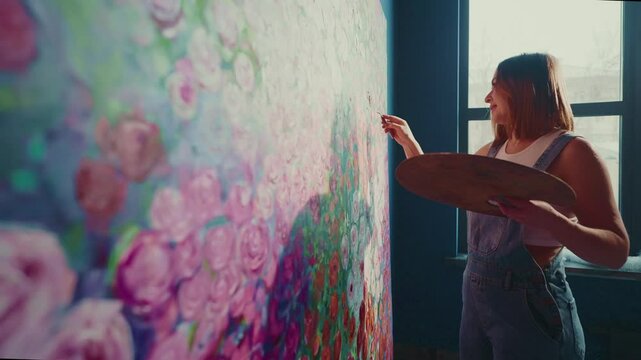 Professional female artist applying final brushstrokes to expansive, vibrant floral canvas, revealing intricate creative process within personal art studio workspace