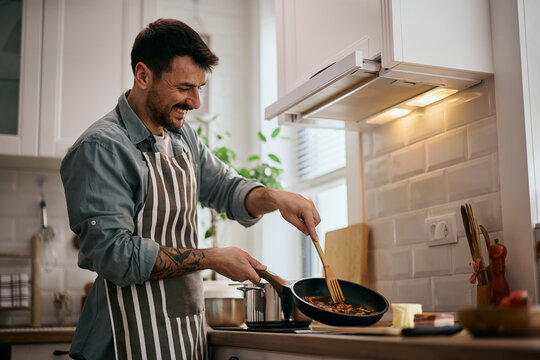 Happy man preparing food in frying pan in kitchen.