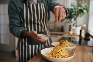 Close up of man serving dish while making pasta in kitchen.