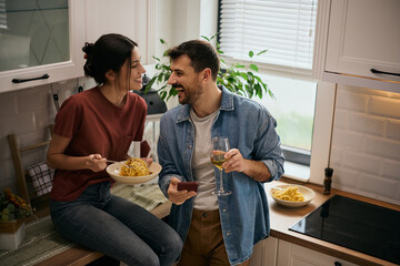 Carefree couple having fun while eating spaghetti in kitchen.