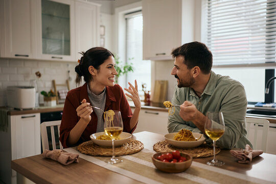 Happy couple communicating while eating pasta at dining table.