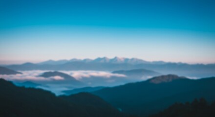 Fototapeta premium A blurred panoramic mountain landscape under a morning sky with clouds and mist unveils the high peaks at dawn