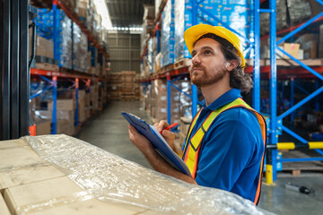 Young worker in blue uniform and safety helmet review inventory record on clipboard. Stand among...