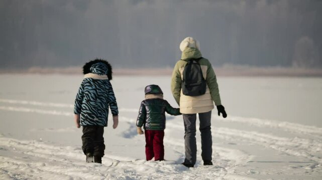 Brave Siberian mother with two daughters trekking across snow-covered gaint lake during extreme cold sunrise. Siberian winter.