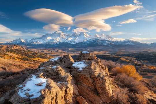 Majestic snow-capped mountains under a dramatic lenticular cloud formation, autumnal valley below. - Powered by Adobe