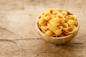 Raw uncooked dried Conchiglie shell pasta. Italian seashells pasta in wooden bowl on wooden background.