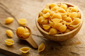 Raw uncooked dried Conchiglie shell pasta. Italian seashells pasta in wooden bowl on wooden background.