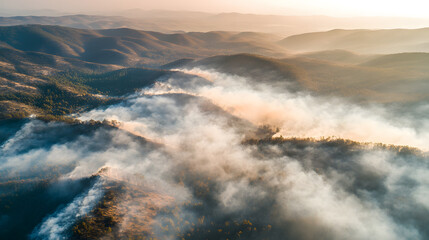 Fototapeta premium Aerial view of wildfire spreading through forested mountain range, with smoke billowing into sky