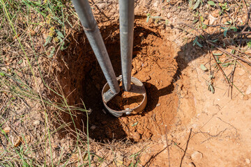Digging a hole with a metal tool in dry, earthy ground.