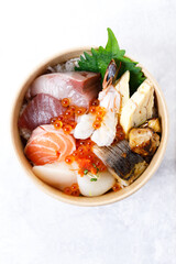 Donburi with sliced of fresh raw seafood and grilled fish on sushi rice in paper container. Healthy take away food.