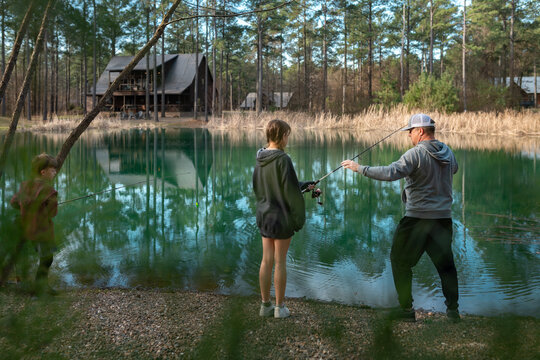 Family fishing together by a forest lake with cabin in background
