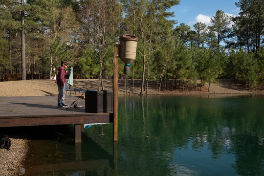 Child fishing from a wooden dock by a forested green pond